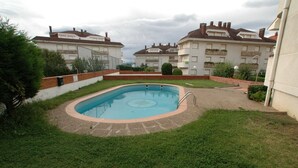 A swimming pool surrounded by a grassy area with a brick border, set against a backdrop of residential buildings.