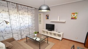 A modern living room with a glass coffee table, a sofa, a TV on a white stand, and a large pendant light.