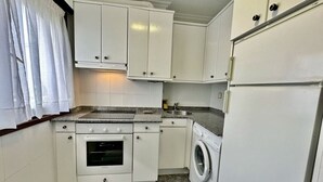 Una cocina compacta con armarios blancos, horno empotrado, lavadora y refrigerador.