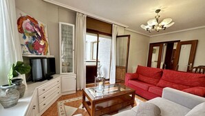 Una sala de estar con una mesa de centro de vidrio, un sofá rojo y un televisor sobre un mueble blanco.
