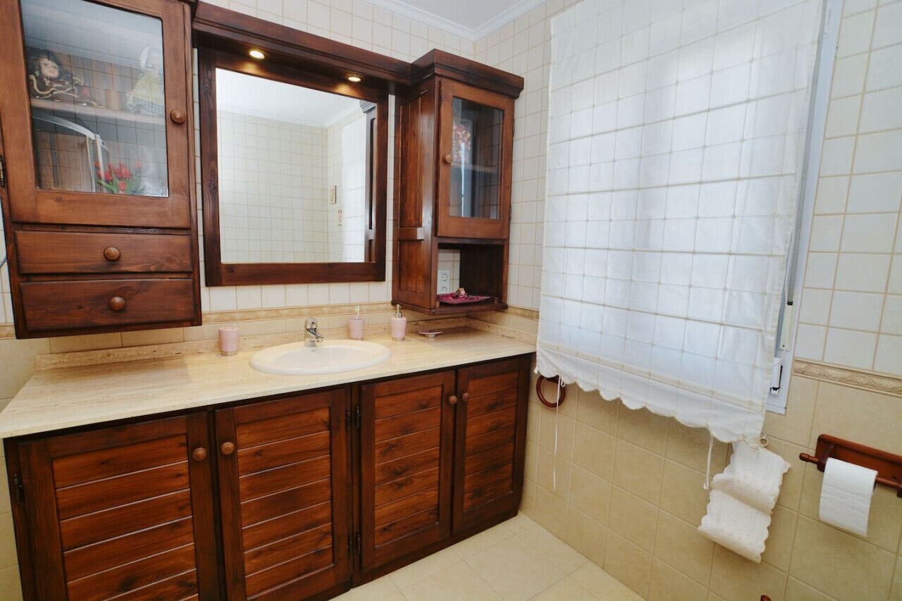 Un baño con tocador de madera, un espejo grande, un lavabo y una cortina de ducha.