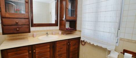 Un baño con tocador de madera, un espejo grande, un lavabo y una cortina de ducha.