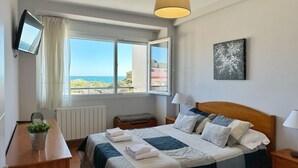 Un dormitorio con cama, mesitas de noche, un escritorio, una silla, una ventana con cortinas, una lámpara y un cuadro en la pared.