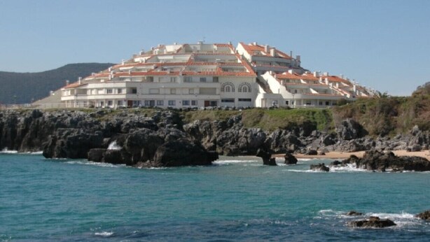 A coastal hotel with multiple balconies, a rocky shoreline, and a clear view of the sea. - Bajo con vistas inigualables - La Caseta 5907 (Isla)