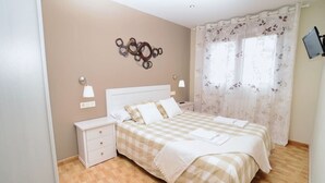 A bedroom with a checkered bedspread, two bedside tables, a wall-mounted TV, and a decorative wall piece. - Bajo con vistas inigualables - La Caseta 5907 (Isla)