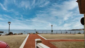 A paved walkway leading to a beach with a red car parked nearby, a lamp post, and a clear view of the sea. - Bajo con vistas inigualables - La Caseta 5907 (Isla)