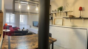 Ein modernes Wohnzimmer mit einem Holzesstisch, einem roten Sofa und einer Küchenzeile mit weißen Schränken und einer schwarzen Arbeitsplatte.