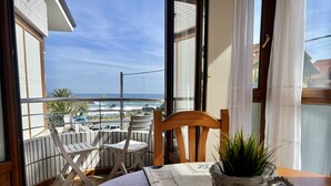 A balcony with a view of the sea, a wooden chair, a table with a plant, and a window with curtains. - Apartamento en Ris con garaje - Pineda 6405 (Noja)