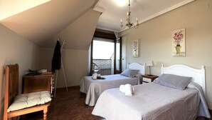A bedroom with two beds, a wooden chair, a small table, a coat rack, and a window with a view. - Apartment close to Ris Beach - Pineda 6606 (Noja)