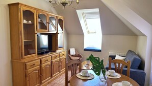 A dining area with a wooden table, chairs, a chandelier, a television on a cabinet, and a view of a blue couch and window. - Apartment close to Ris Beach - Pineda 6606 (Noja)