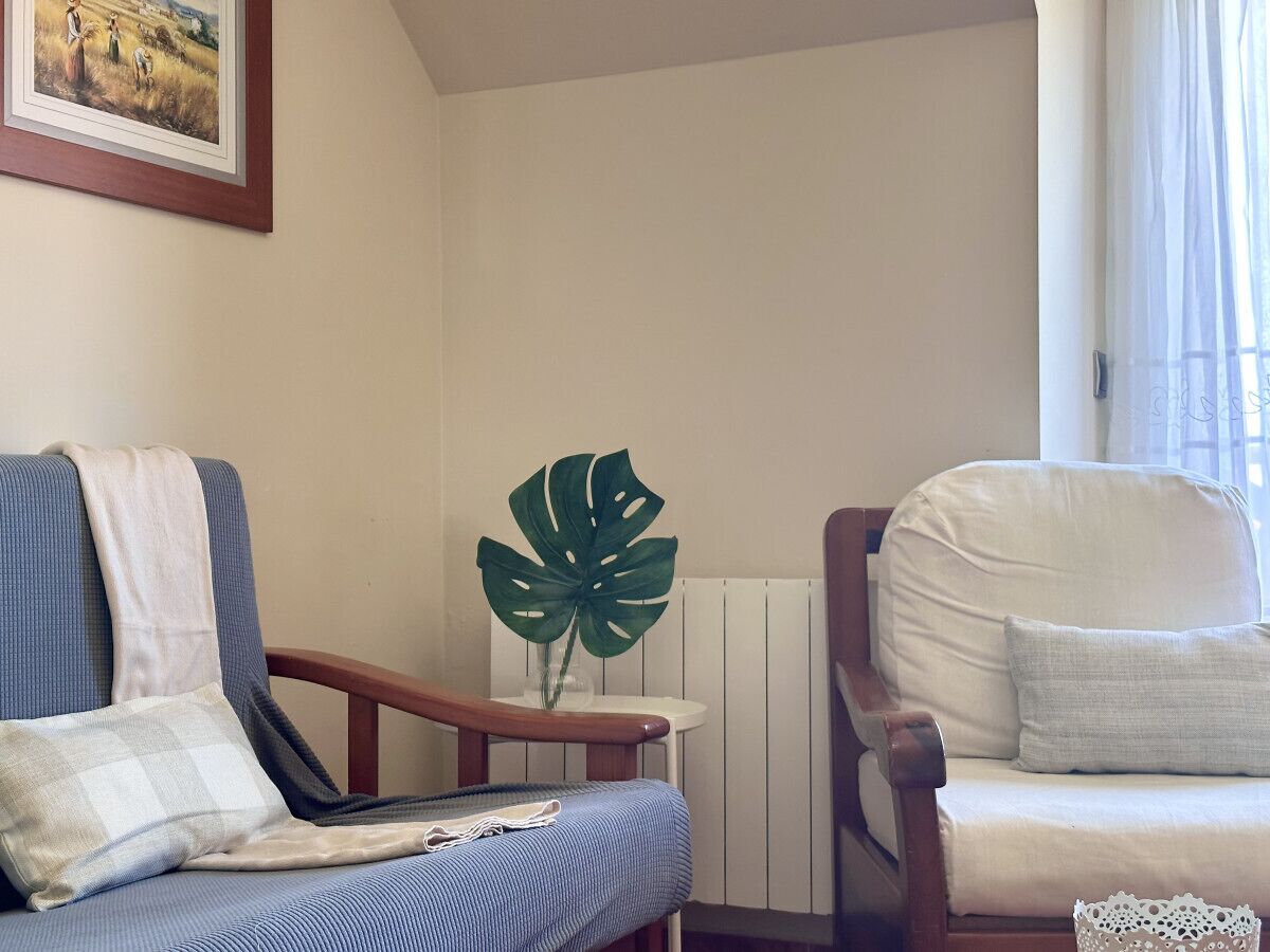 Un salon avec un canapé bleu, un fauteuil blanc, une table d’appoint en bois ornée d’une plante et un tableau encadré accroché au mur.