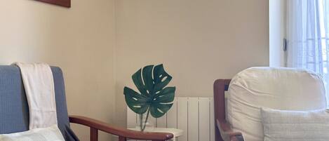 Un salon avec un canapé bleu, un fauteuil blanc, une table d’appoint en bois ornée d’une plante et un tableau encadré accroché au mur.