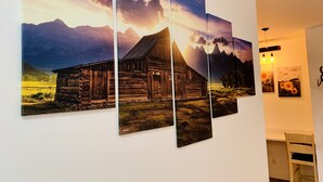 A wall with four framed paintings depicting a rustic barn and mountains.