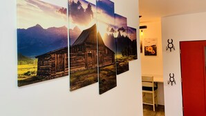 A hallway with a wooden cabin painting, a red door, and a white wall with a black symbol.