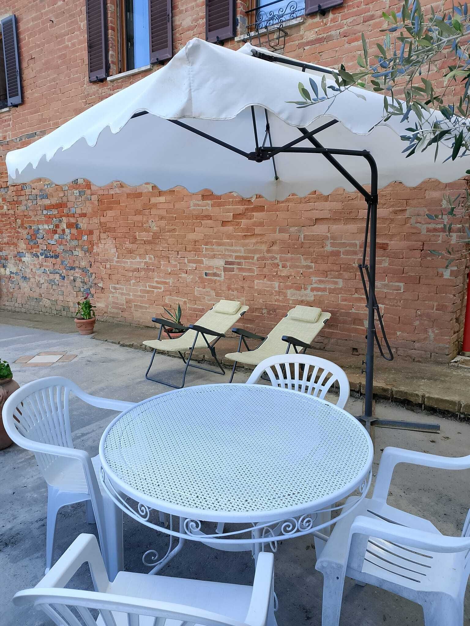 A round outdoor table with white chairs and a white umbrella providing shade.