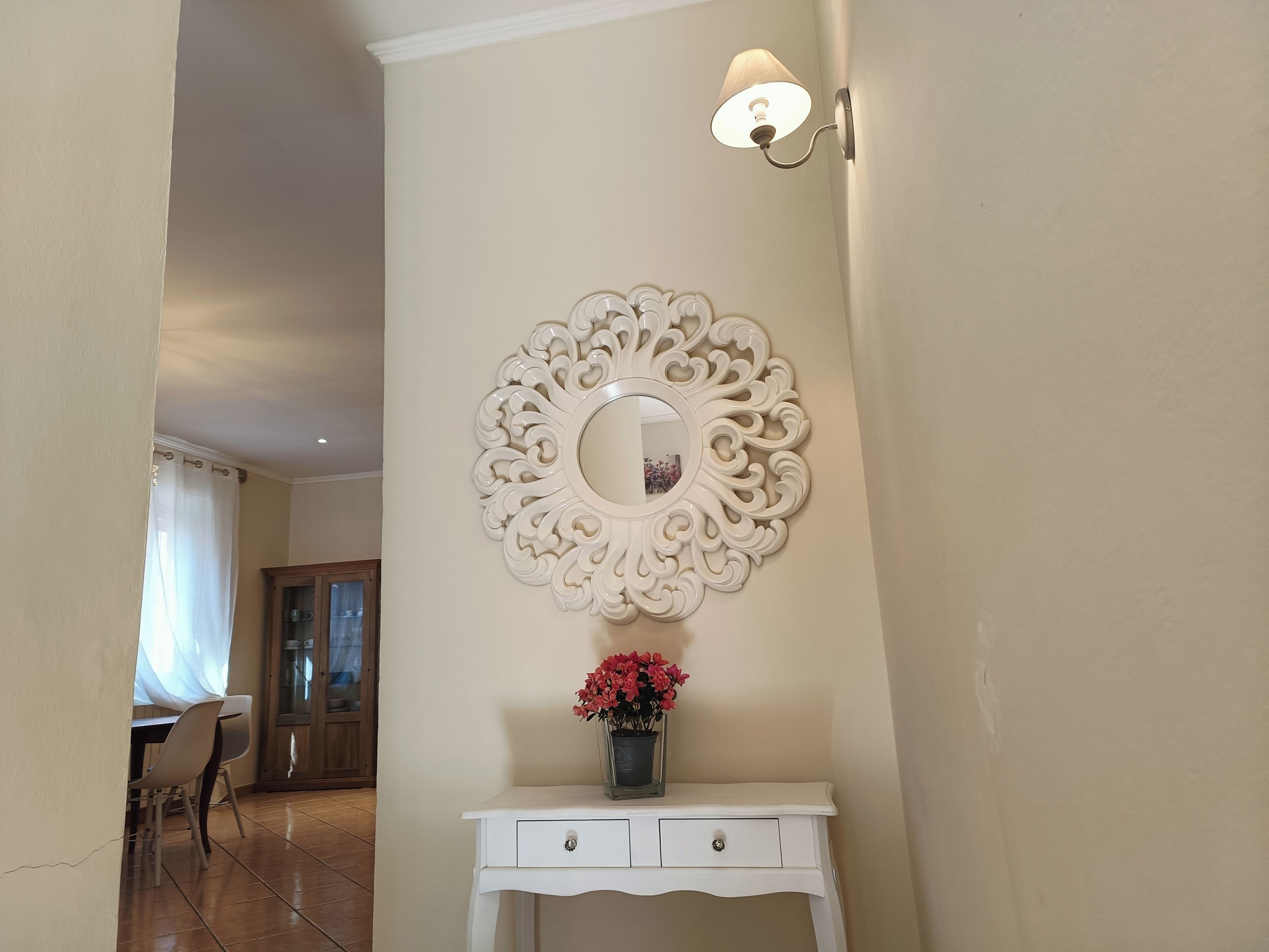 A hallway with a white console table, a decorative mirror, and a wall-mounted light fixture.