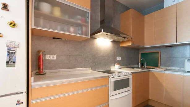 Eine kleine Küche mit Holzausstattung, einem eingebauten Backofen und einer Edelstahl-Dunstabzugshaube.