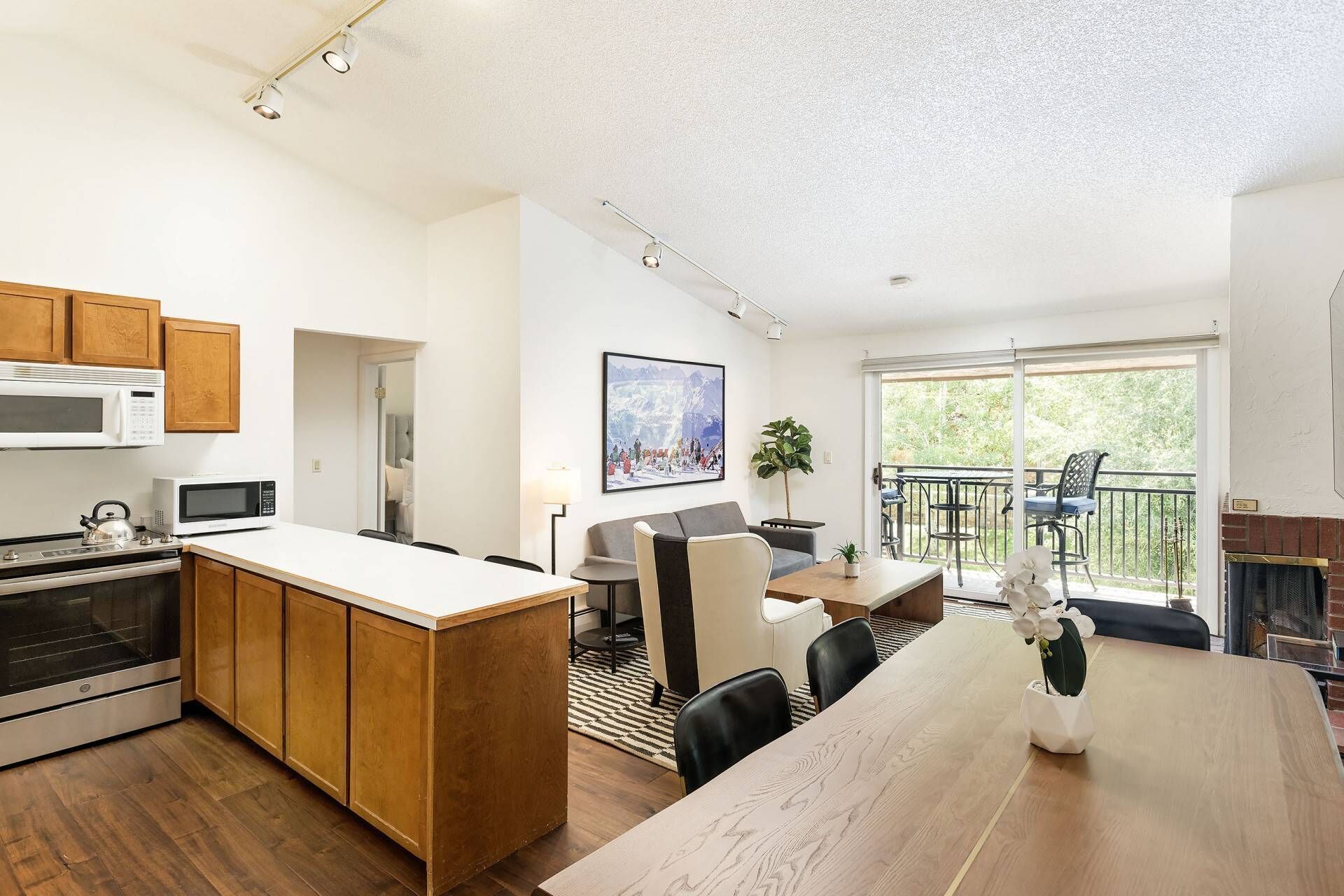 A modern kitchen with wooden cabinets, a central island, and a dining area with a view of the outdoors.