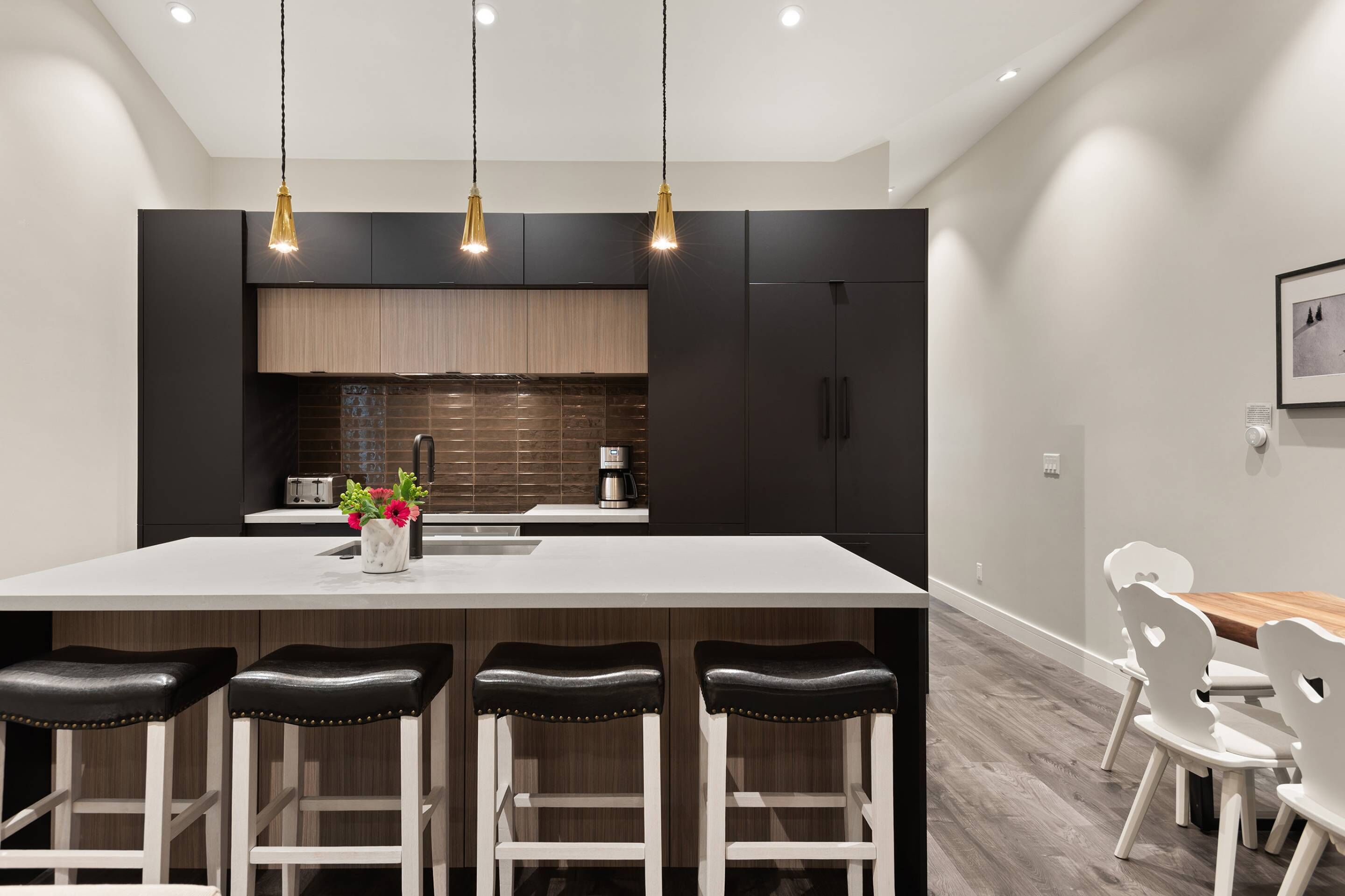 Una cocina moderna con armarios oscuros, una isla blanca con taburetes y luminarias colgantes.