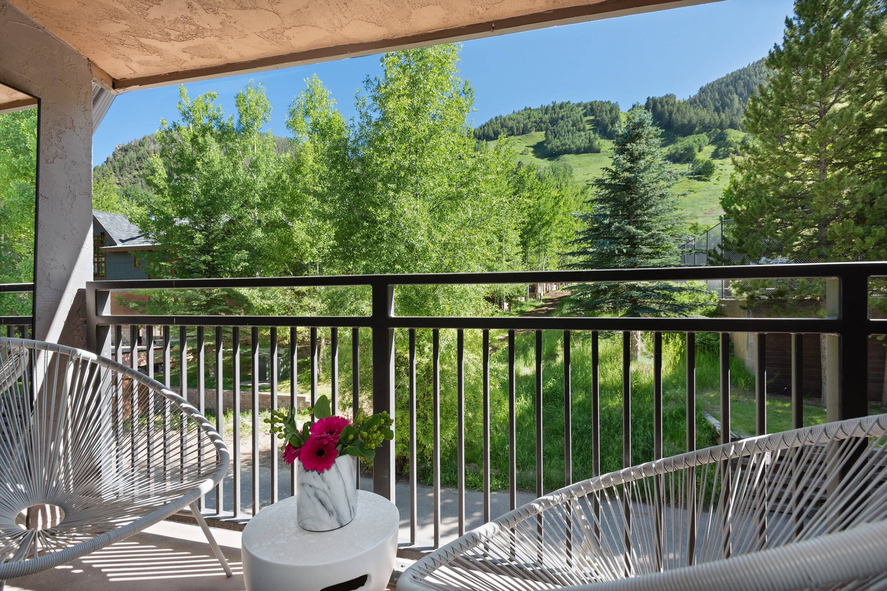 Een balkon met witte wicker stoelen en een tafeltje met een bloevas.