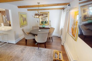 Un coin repas comprenant une table ronde, quatre chaises, un lustre et un grand miroir au mur.