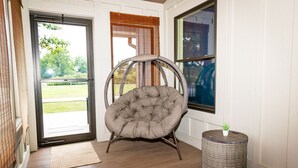 A room with a large window, a wicker chair, and a small round table with a plant. - Welcome Race Fans! - Oversize Parking - Firepit - Mural - West Indy - Brownsburg (Indianapolis)