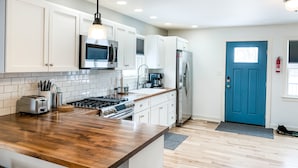 A modern kitchen with white cabinets, a wooden countertop, a stainless steel stove, and a blue door. - Welcome Race Fans! - Oversize Parking - Firepit - Mural - West Indy - Brownsburg (Indianapolis)