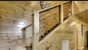 Un escalier en bois avec une rampe en métal, une horloge murale et une grille d’aération.