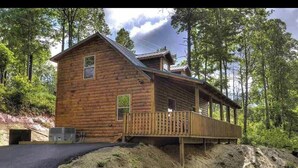 Une cabane en rondins dotée d’une véranda, entourée d’arbres.