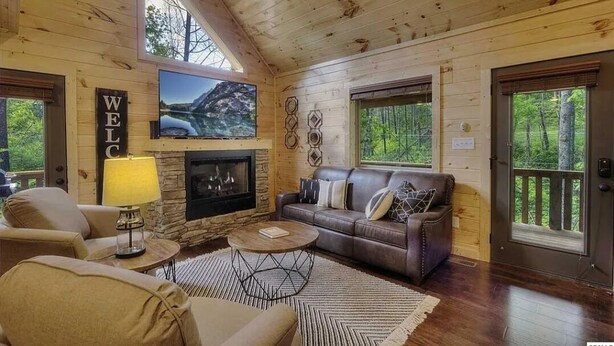 Un intérieur de chalet chaleureux avec une cheminée en pierre, un canapé en cuir et une pancarte indiquant « BIENVENUE ».