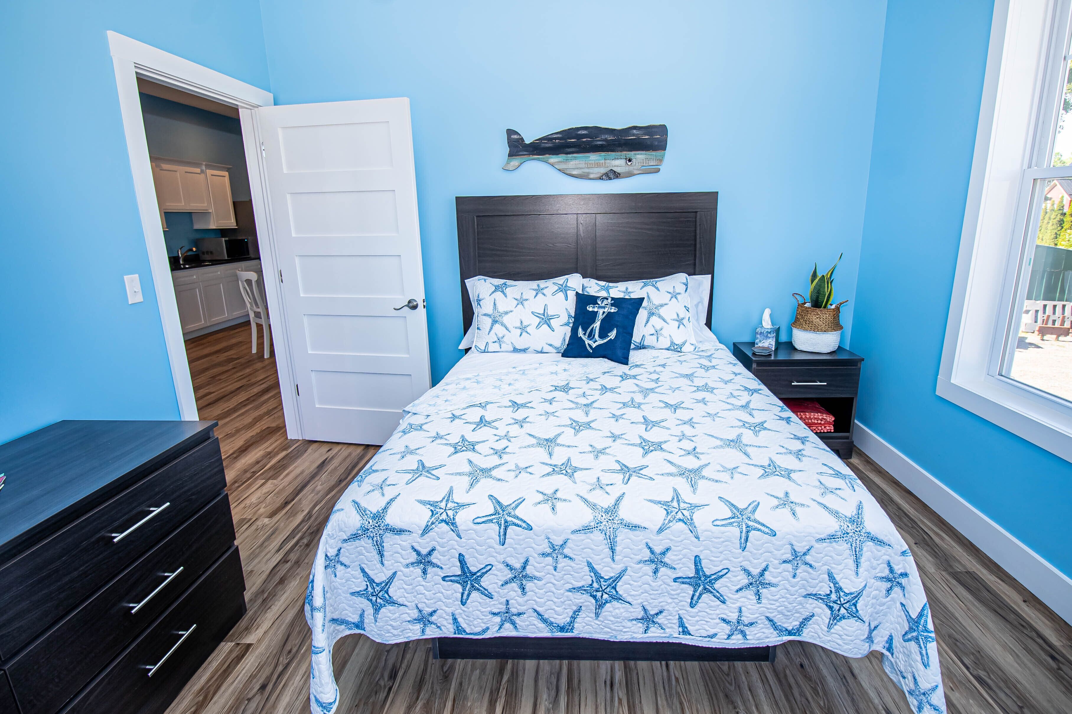 Une chambre à coucher comprenant un lit, une table de chevet, une commode, un décor mural représentant des poissons et une fenêtre.