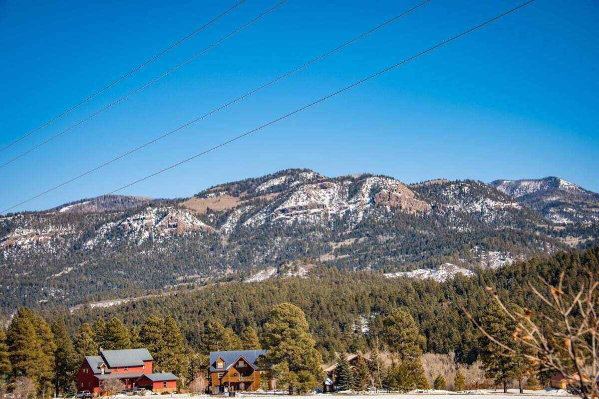 Paisaje de montaña con un edificio rojo en primer plano y una cadena montañosa nevada al fondo.