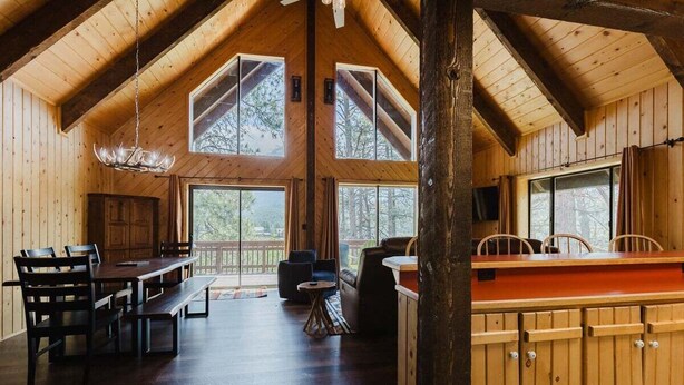 A spacious wooden cabin with a high ceiling, large windows, a dining area with a long table and chairs, a seating area with a sofa and chairs, and a kitchen area with wooden cabinets. - Close to Wolf Creek, Fish San Juan River, Escape the Crowds (Pagosa Springs)