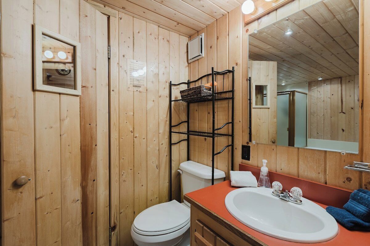 A wooden bathroom with a white toilet, a sink with an orange countertop, and a mirror above the sink.