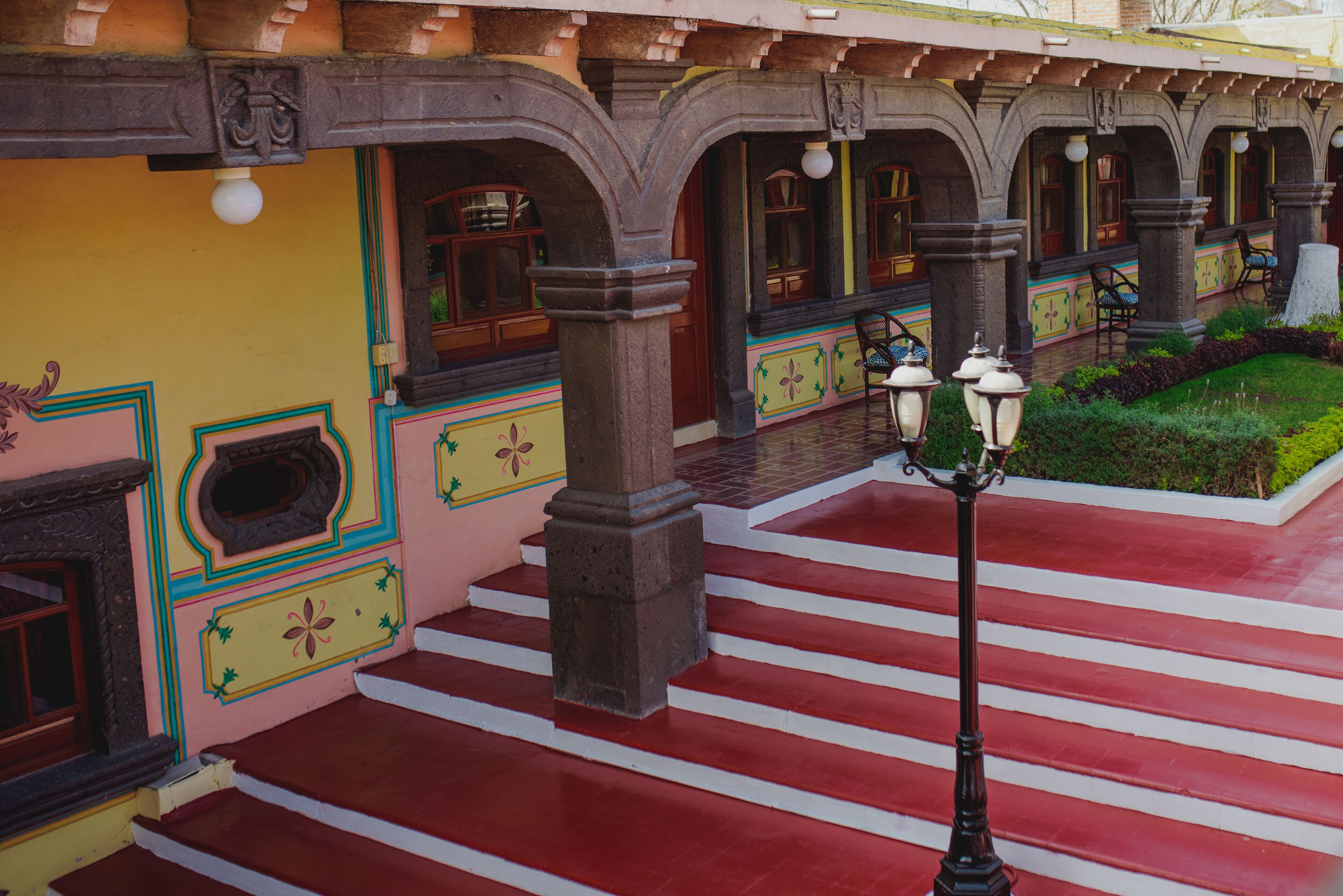 A covered outdoor area with a red and white striped floor, stone columns, and a lamp post.
