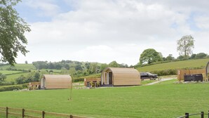 A rural setting with two wooden cabins, a dining area, and a car parked nearby. - 1 bedroom accommodation in Llanfyllin, near Welshpool (Llanfyllin, near Welshpool)