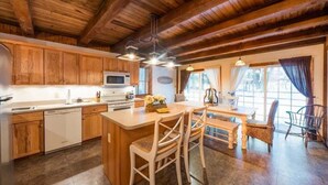 A rustic kitchen with wooden cabinets, a central island with stools, a dining table, and a large window with curtains. - 2 bedroom, 1.5 baths, full kitchen, comfortable living space with free parking (Palmyra)