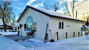 A single-story house with a large garage door, a covered porch, and a snow-covered yard. - Remodeled, Grill, Outside Seating, Dock, Swimming (Brainerd)