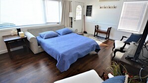 Un dormitorio con cama, mesita de noche, lámpara, silla, escritorio y computadora.