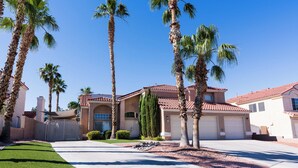 A residential house with a red-tiled roof, a garage, and a well-maintained lawn with palm trees.