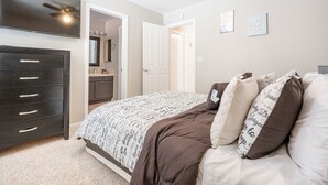 A bedroom with a bed, a dresser, a vanity, and a ceiling fan.