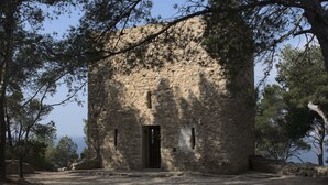 An ancient stone building with a central door, surrounded by trees.