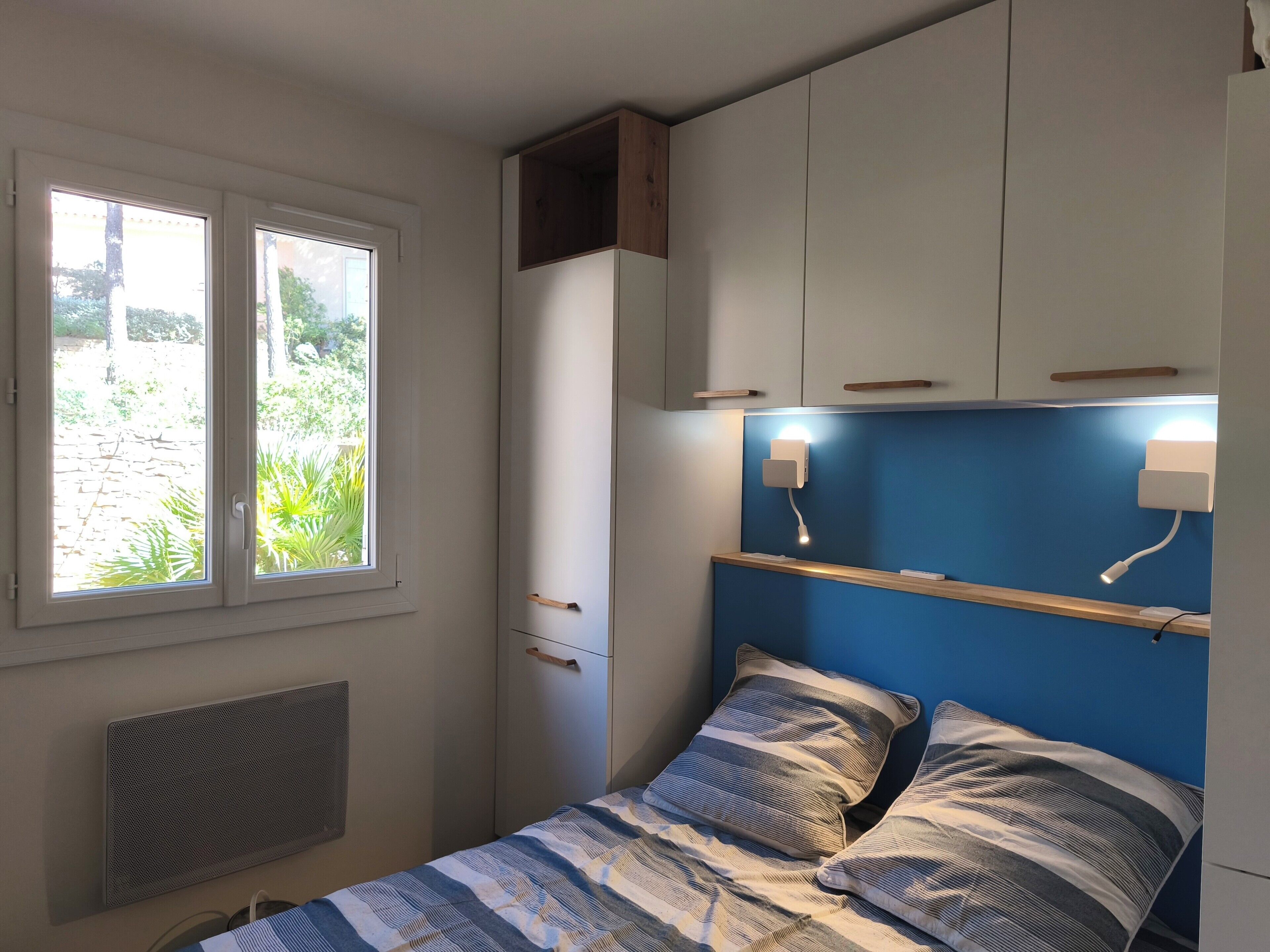 Une chambre à coucher comprenant un lit, une fenêtre, une armoire et un luminaire fixé au mur.