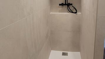 Un área de ducha pequeña y cerrada, con ducha empotrada en el techo, paredes de azulejos y suelo de madera.