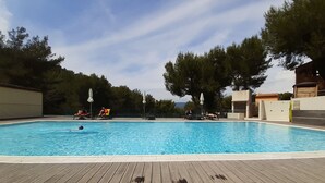 A swimming pool with a wooden deck, surrounded by trees and umbrellas.