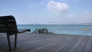 A wooden deck with a bench overlooking a calm sea and distant cityscape.