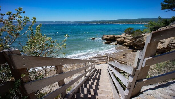 A wooden staircase leading to a beach with clear blue water and rocky outcrops.