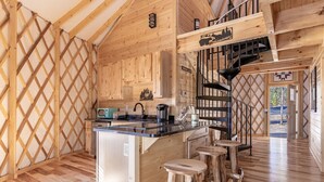 A wooden cabin interior with a kitchen area, wooden stools, and a staircase. - Luxury Yurt Cozy & Fun 1br/1bth, experience it, Private Deck w Grill & HotTub (Pigeon Forge)
