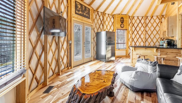 A cozy cabin interior with a kitchen area, a dining table, and a seating area with a log table and cushions. - Luxury Yurt Cozy & Fun 1br/1bth, experience it, Private Deck w Grill & HotTub (Pigeon Forge)