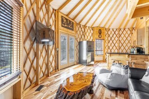 A cozy cabin interior with a kitchen area, a dining table, and a seating area with a log table and cushions. - Luxury Yurt Cozy & Fun 1br/1bth, experience it, Private Deck w Grill & HotTub (Pigeon Forge)